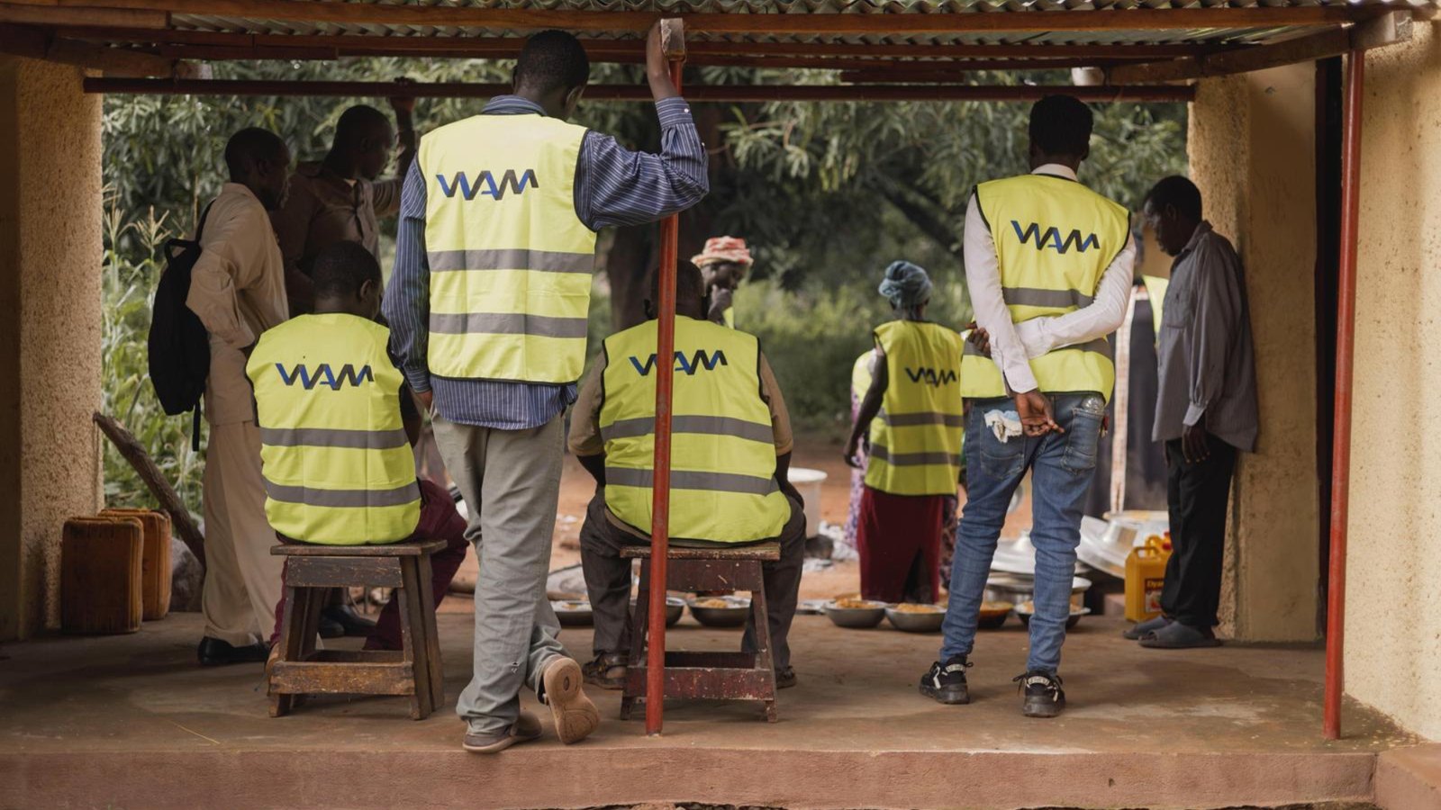 WAM workers in high visibility vests serving bowls of hot food to people seated under a shelter
