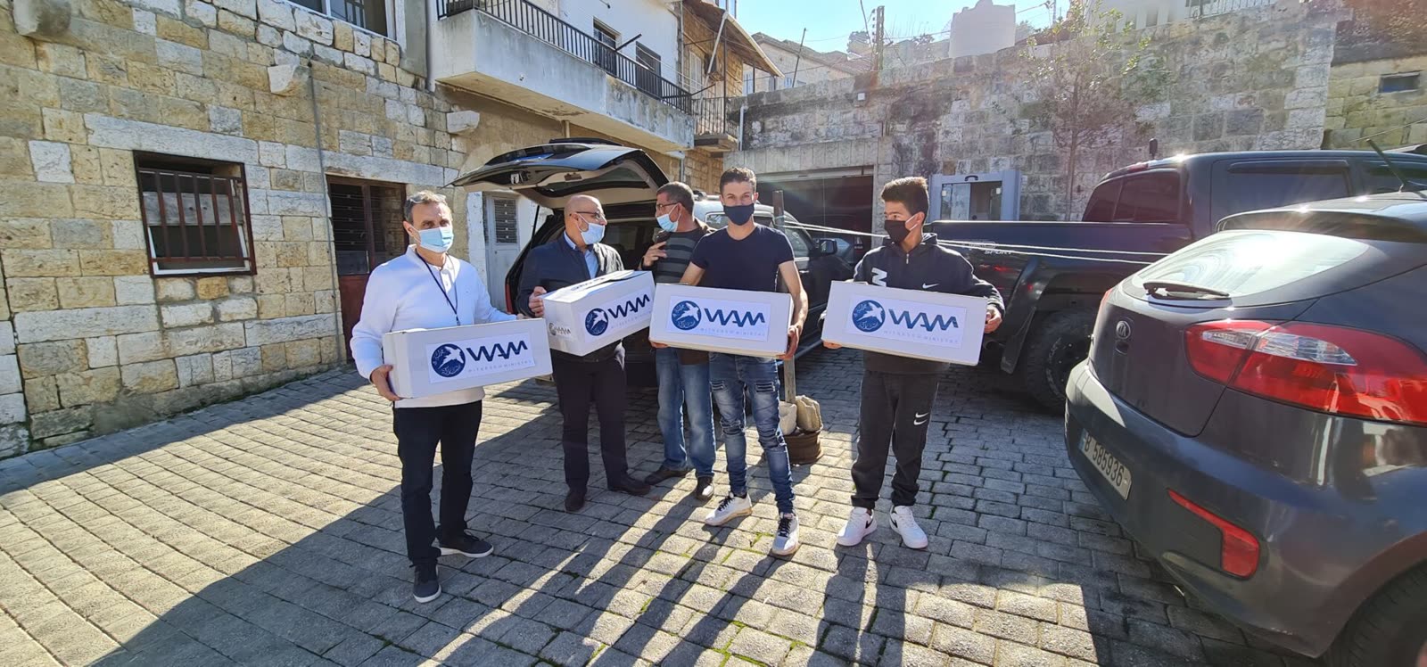 WAM staff carrying relief parcels along a stone street in a Lebanese village